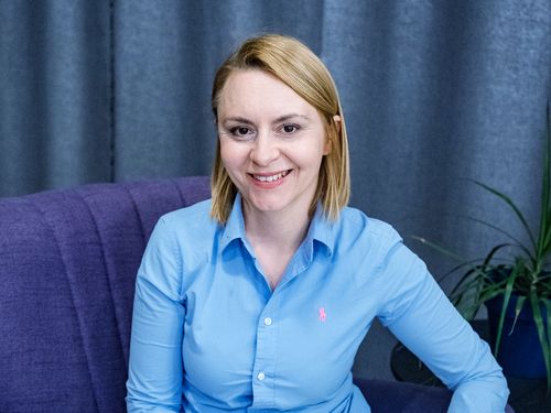 Prezeska Centrum Wsparcia  - Marta Gawryluk siedzi na fotelu i się uśmiecha. Jest ubrana w niebieską koszulę. 