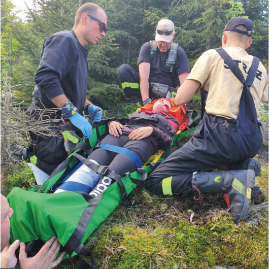Trzech mężczyzn jest pochylonych na osobą, która jest zapięta do maty Rescue.